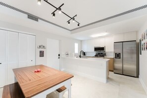 Une cuisine moderne avec des meubles blancs, une table à manger en bois et un réfrigérateur en acier inoxydable.
