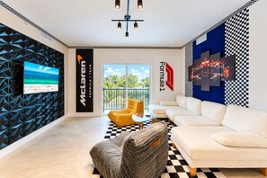 Un salon moderne avec un sol à carreaux, un canapé, un fauteuil jaune, un téléviseur et un mur orné de motifs géométriques et du logo de la Formule 1.
