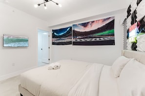 Een moderne slaapkamer met een groot bed, een flatscreen televisie aan de muur en twee levendige kunstwerken.