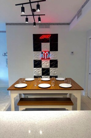 Een eetruimte met een houten tafel voor zes personen, een moderne lamp erboven en een decoratief wandpaneel met een geruit patroon.