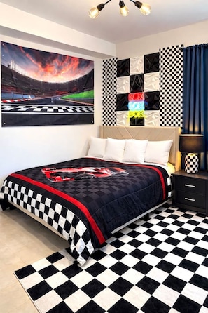 Een slaapkamer met een zwart-witte vloer, een bed met een sprekend bedovertrek met raceauto's, een muur met een muurschildering van een racebaan en een schilderij met een zwart-wit patroon.