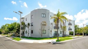 A modern multi-story building with a flat roof, surrounded by greenery and a clear sky. - Luxe F1 3BR | Steps to Design District & Wynwood (Miami)