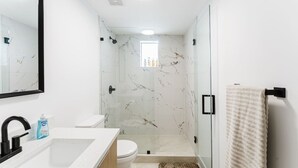 A modern bathroom with a glass shower enclosure, a white sink, and a toilet. - Luxe F1 3BR | Steps to Design District & Wynwood (Miami)