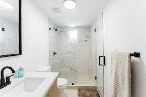 Een moderne badkamer met een douchecabine van glas, een wit wastafelmeubel en een toilet.