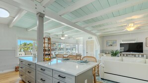 A spacious living area with a large white sofa, a dining table with chairs, a kitchen area with a refrigerator, and a ceiling fan. - Palmetto Breeze (Fort Myers Beach)