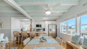 A spacious kitchen with white cabinets, a stainless steel refrigerator, and a dining area with a wooden table and chairs. - Palmetto Breeze (Fort Myers Beach)