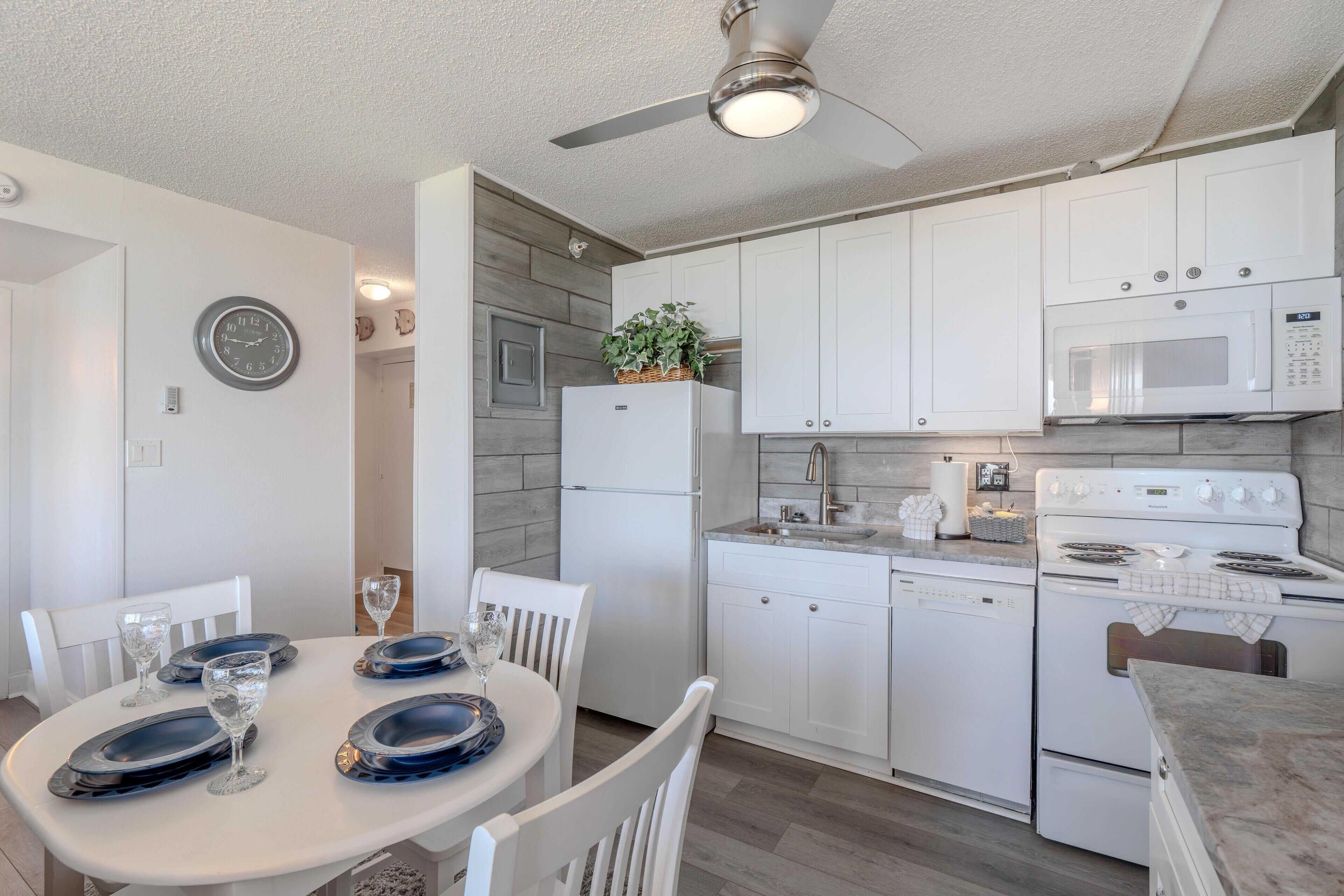 A modern kitchen with white cabinets, a microwave, an oven, and a dining table set with plates and glasses.