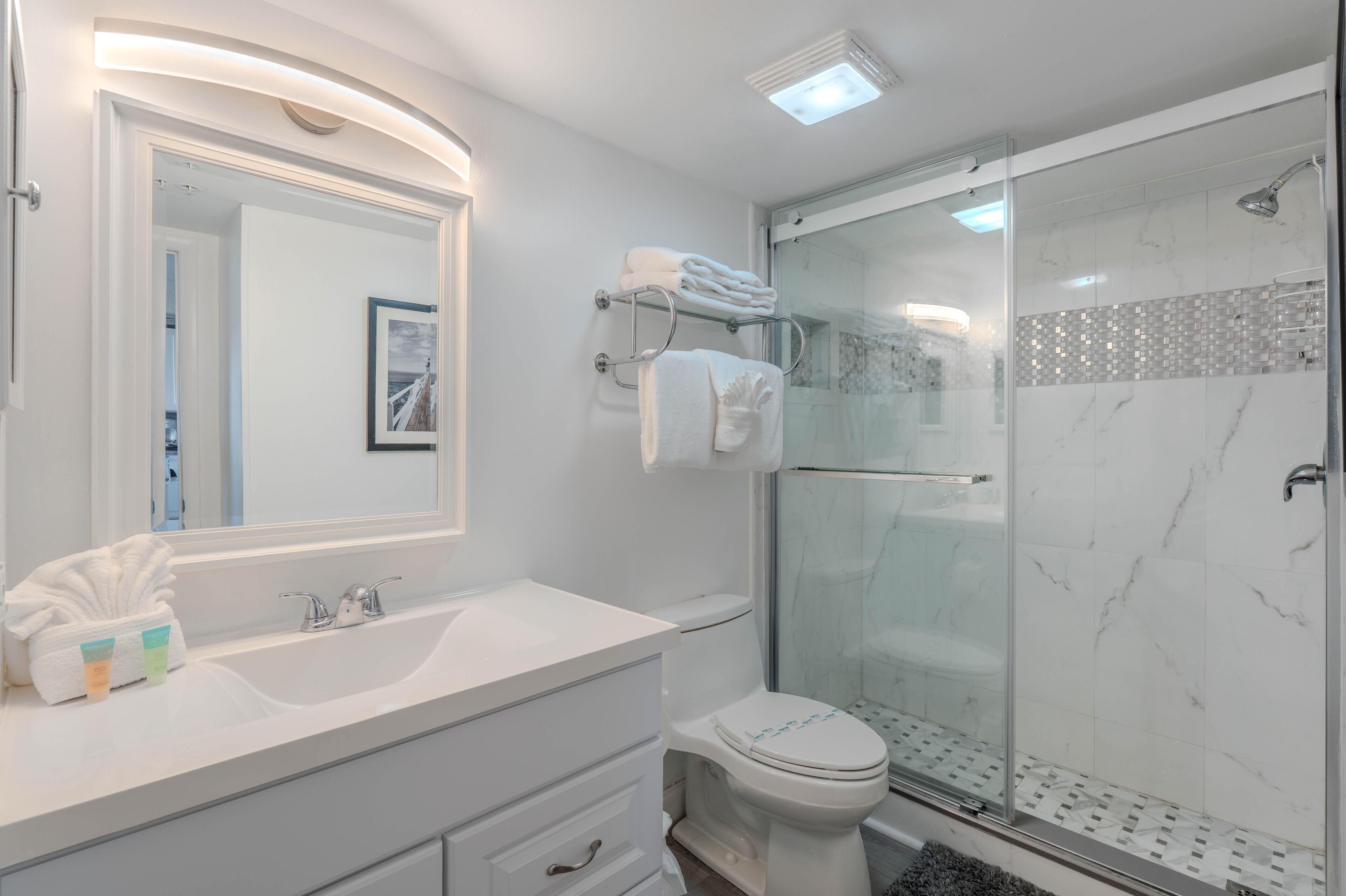 A modern bathroom with a glass shower enclosure, a white sink, and a large mirror.