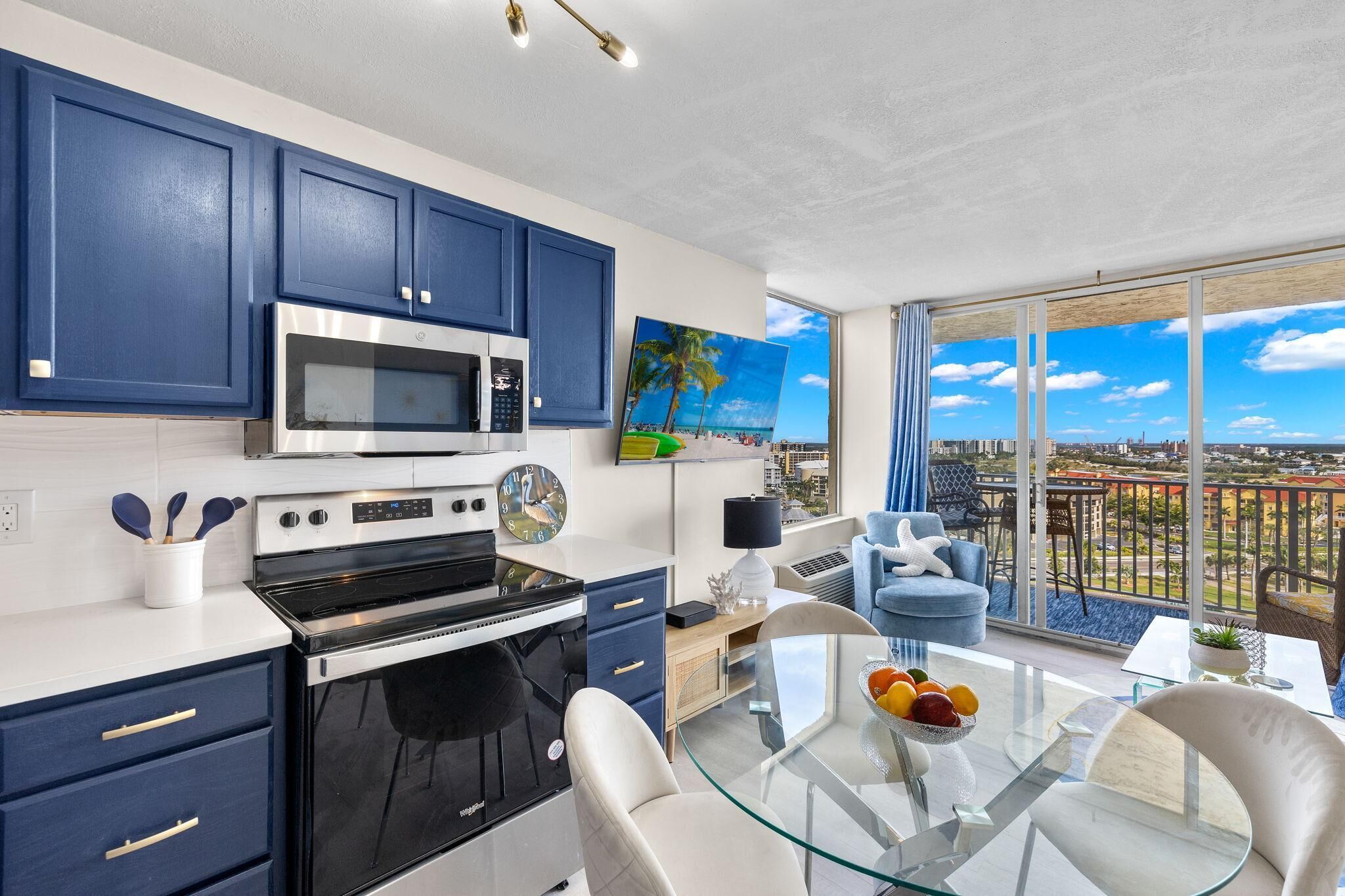 A modern kitchen with a large window, a dining area with a glass table, and a balcony with a city view.