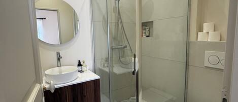 Un baño moderno con cabina de ducha de vidrio, un lavabo blanco y un inodoro.