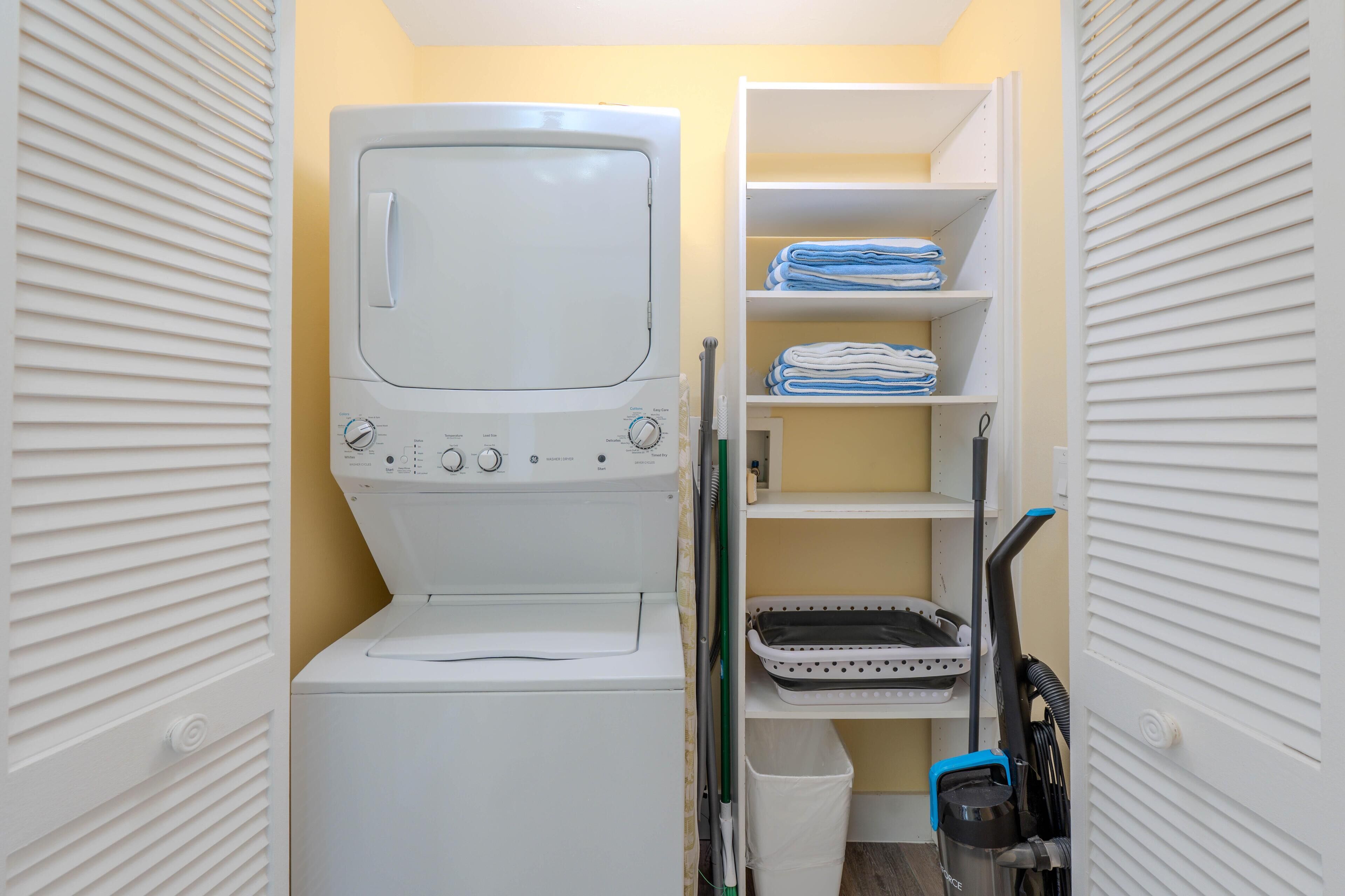 A laundry room with a washing machine, shelves with folded towels, and cleaning supplies.