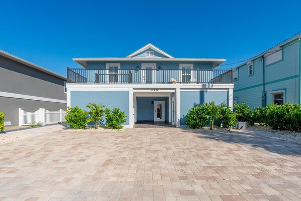 A two-story building with a balcony, a driveway, and a white fence. - 218 Mermaid Beach House (Fort Myers Beach)
