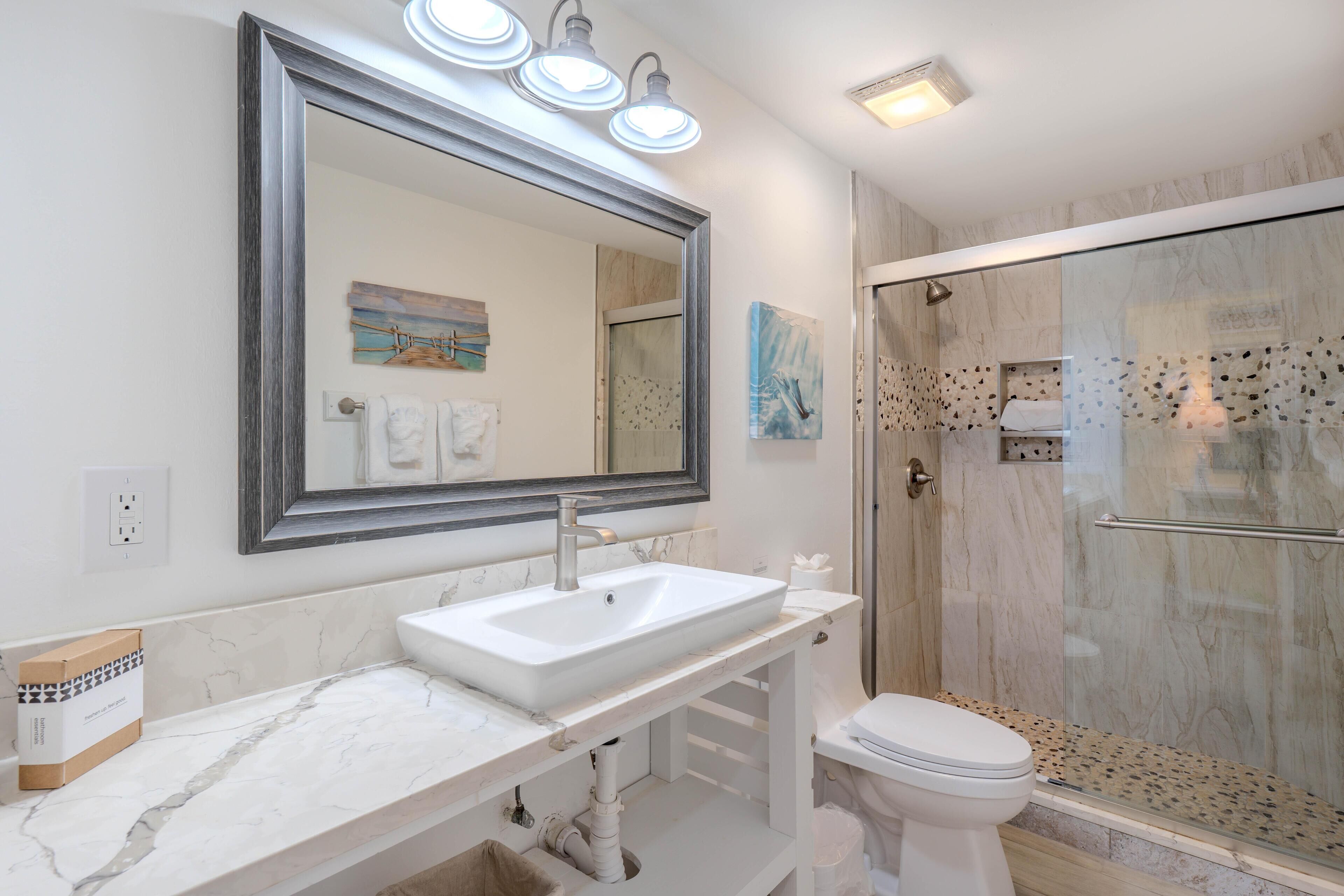 A bathroom with a marble sink, a toilet, a glass-enclosed shower, and a large mirror.