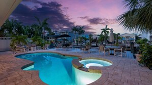 A swimming pool with lounge chairs and umbrellas, surrounded by palm trees and buildings. - 218 Dolphin Beach House (Fort Myers Beach)