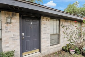 A house with a dark front door, stone walls, a window with blinds, and potted plants.