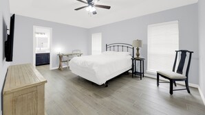 Ein Schlafzimmer mit Bett, Schreibtisch, Stuhl, Deckenventilator und Fenster mit Jalousien.
