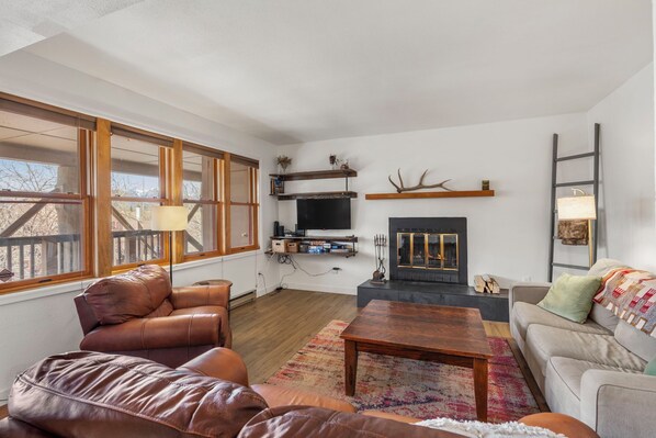Un salon avec une cheminée, un canapé en cuir, une table basse en bois et un téléviseur posé sur une étagère.