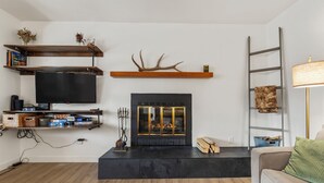 A living room with a fireplace, television, shelves, and a ladder.