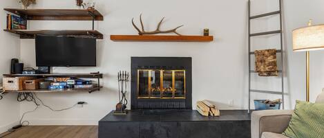 A living room with a fireplace, television, shelves, and a ladder.