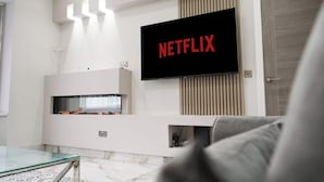 Una sala de estar moderna con un televisor de pantalla plana montado en la pared que muestra 'NETFLIX', una mesa de centro de vidrio y una chimenea.