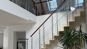 Un interior moderno con una escalera, barandas de vidrio y una planta en maceta.