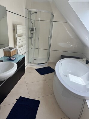 A modern bathroom with a glass shower enclosure, a large bathtub, and a white sink.