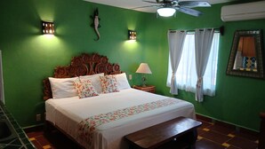 Une pièce comprenant un lit, un ventilateur de plafond, une lampe fixée au mur et une fenêtre avec des rideaux.