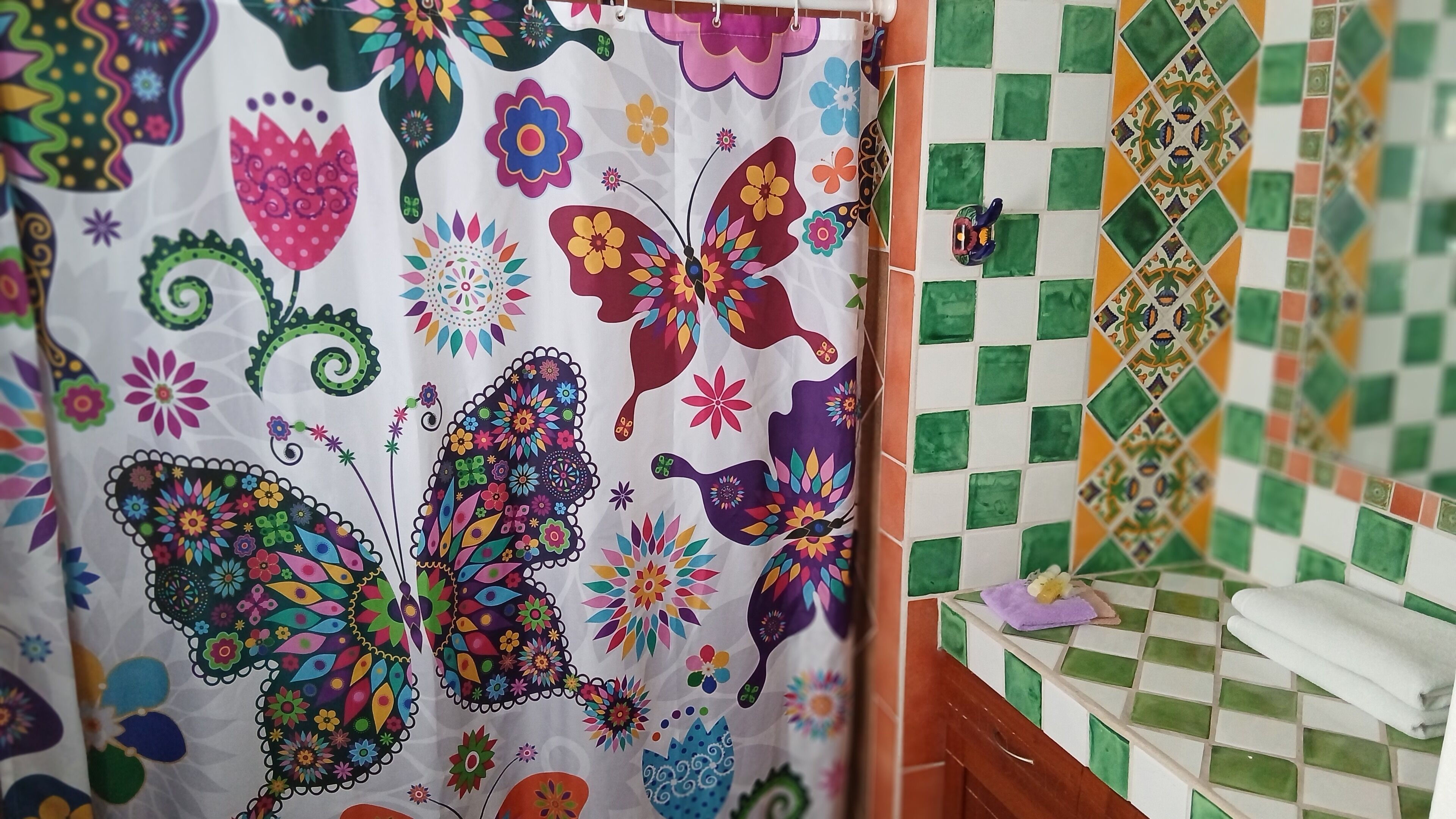 Un baño con cortina de ducha colorida, pared con azulejos y una toalla sobre la encimera.