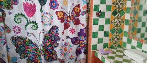 Un baño con cortina de ducha colorida, pared con azulejos y una toalla sobre la encimera.