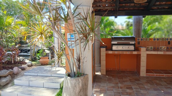 An outdoor patio with a barbecue grill, potted plants, and a tiled floor.