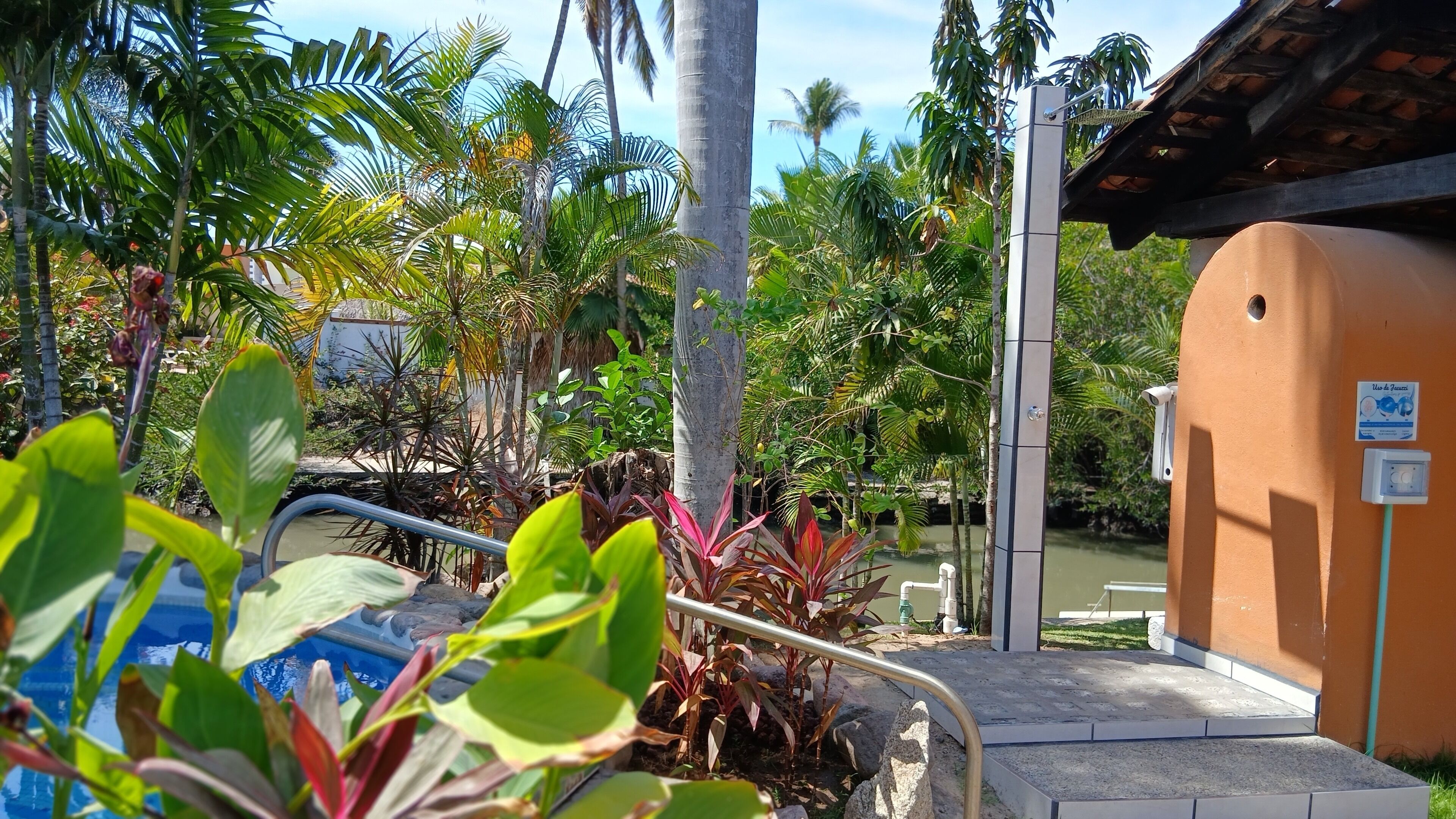 A pool area with a water slide, surrounded by tropical plants and a small building with a sign.