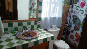 Une salle de bain avec un mur recouvert de carreaux à motifs à carreaux, un lavabo coloré, des toilettes et un rideau de douche orné de motifs floraux.