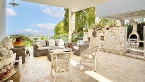 A covered outdoor seating area with wicker furniture, a stone wall, and a view of the landscape. - Ostuni Green Hills App. 2 - Panoramic view, charm, veranda and shared jacuzzi (Puglia)
