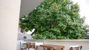 Eine Terrasse mit Tisch und Stühlen, ein großer Baum mit grünen Blättern und gelben Früchten sowie eine weiße Wand.