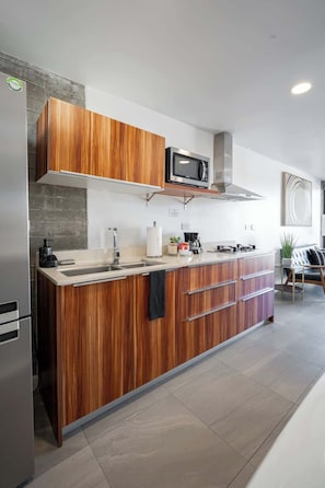 Een moderne keuken met houten kastjes, een roestvrijstalen koelkast, een magnetron en een koffiezetapparaat.
