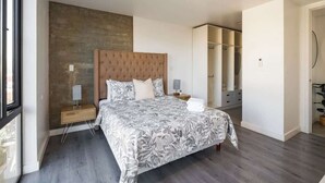 A modern bedroom with a large bed, a wooden headboard, a nightstand, a bedside table, and a wardrobe. - Revolucion Border - Stylish Downtown Suite (Tijuana)