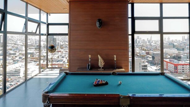 A pool table in a room with large windows, a wooden ceiling, and a city view. - Revolucion Border - Stylish Downtown Suite (Tijuana)