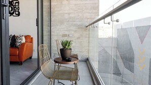 A balcony with a sofa, a chair, a small table, and a potted plant. - Revolucion Border - Stylish Downtown Suite (Tijuana)