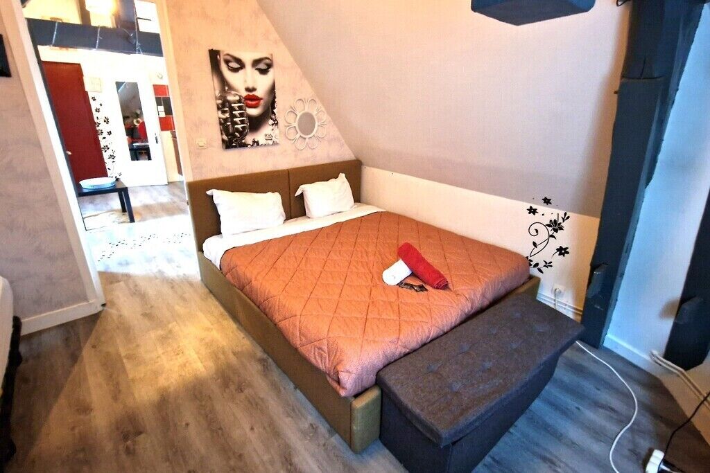 A bedroom with a bed, a bench, a wall with a floral design, and a door leading to another room.