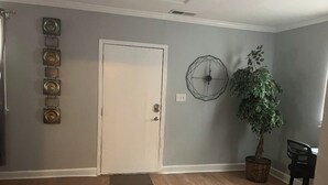 A room with a wooden floor, a white door, a wall-mounted decorative piece, a potted plant, and a black office chair. - Serene 3-bedroom house in a pleasant Atlanta neighborhood. (Atlanta)