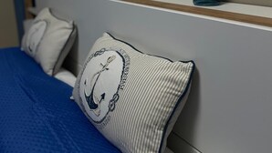 Un lit avec une literie bleue, un oreiller orné d’un motif marin et un vase décoré d’un motif de poisson, posé sur une table de chevet.