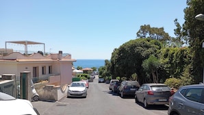 Une rue étroite, bordée de voitures garées et d’immeubles, qui mène à un point de vue sur la mer.