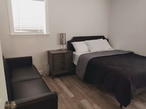 A bedroom with a bed, a nightstand, a lamp, a bench, and a window.