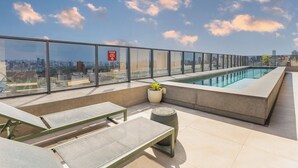 A rooftop terrace with a swimming pool, lounge chairs, and a city view. - Piscina Gym & Rooftop no Jardins - Luxo (São Paulo)