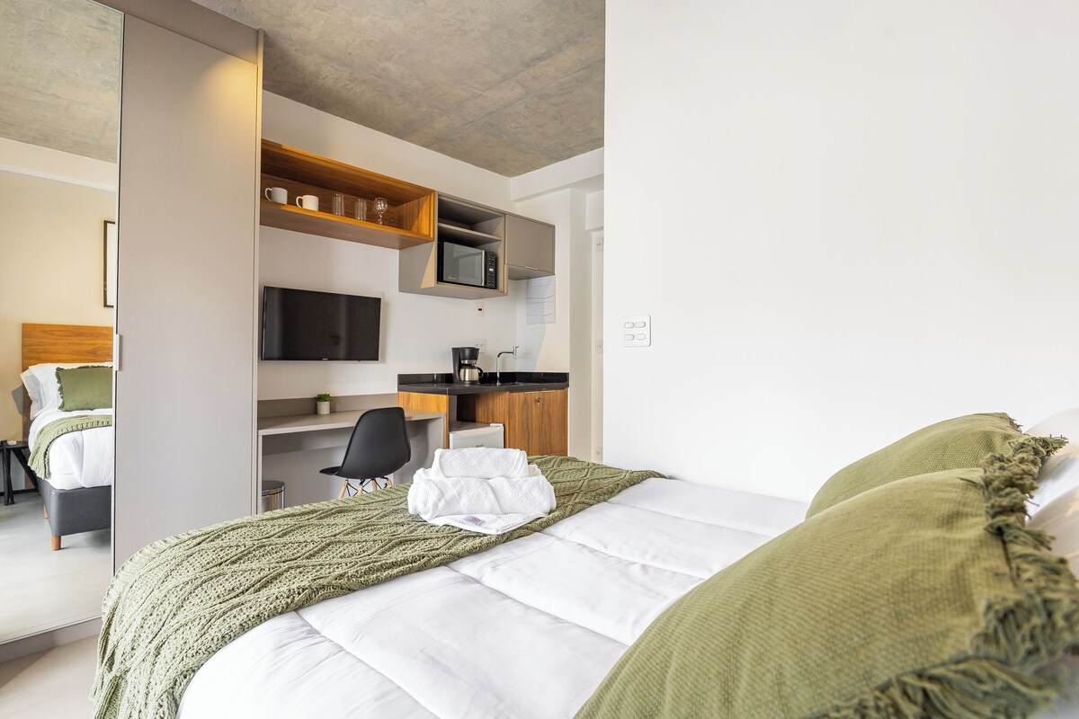 Quarto de hotel com cama, escrivaninha, televisão e micro-ondas.