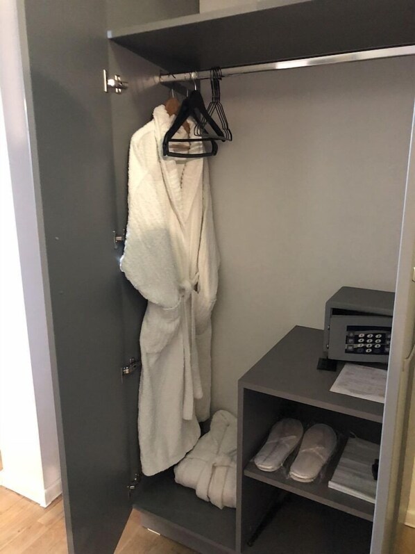 Un armari amb porta corredissa on es pot veure una bata penjada en un penjador, una calaixera de sabates amb xancles i un petit aparell electrònic damunt d'una taula.