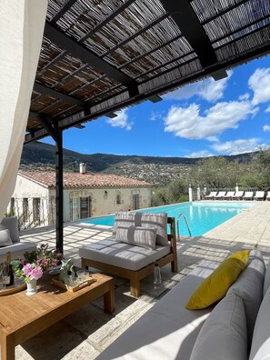 A poolside area with a sofa, a table with drinks, and a view of a swimming pool and distant landscape. - Villa Notre-Dame-des-Fleurs - Luxury in Provence, 6 bedrooms, large pool (Grasse)