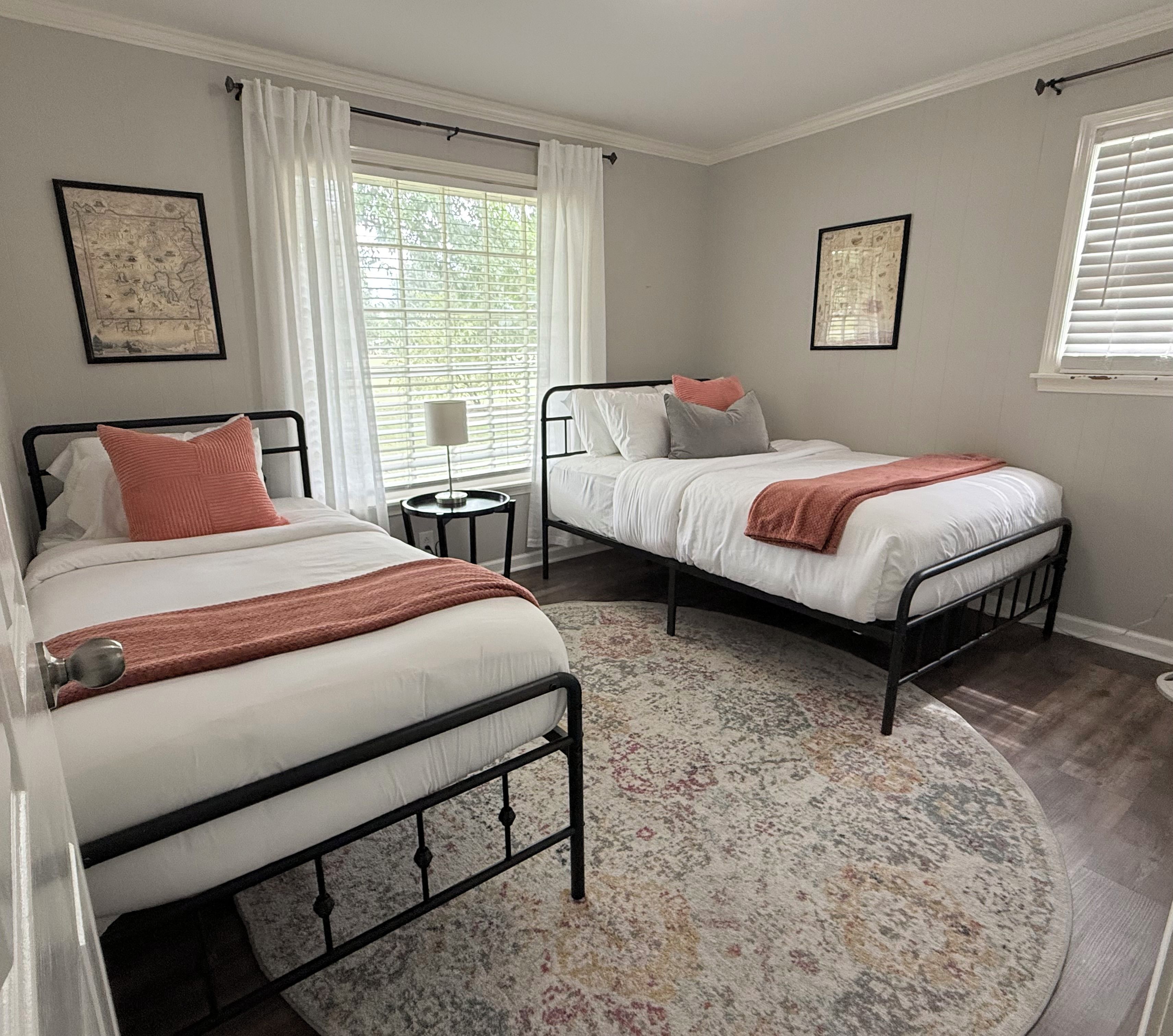 A bedroom with two beds, a round rug, and a window with curtains.