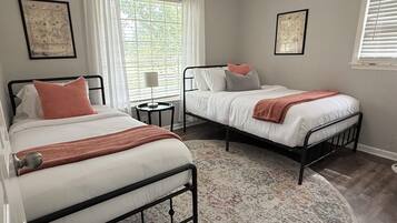 A bedroom with two beds, a round rug, and a window with curtains.