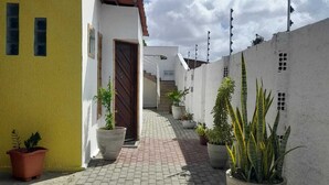 A paved courtyard with potted plants, a white building with a brown door, and a clear sky. - Pousada Terrissol (São Gonçalo do Amarante)